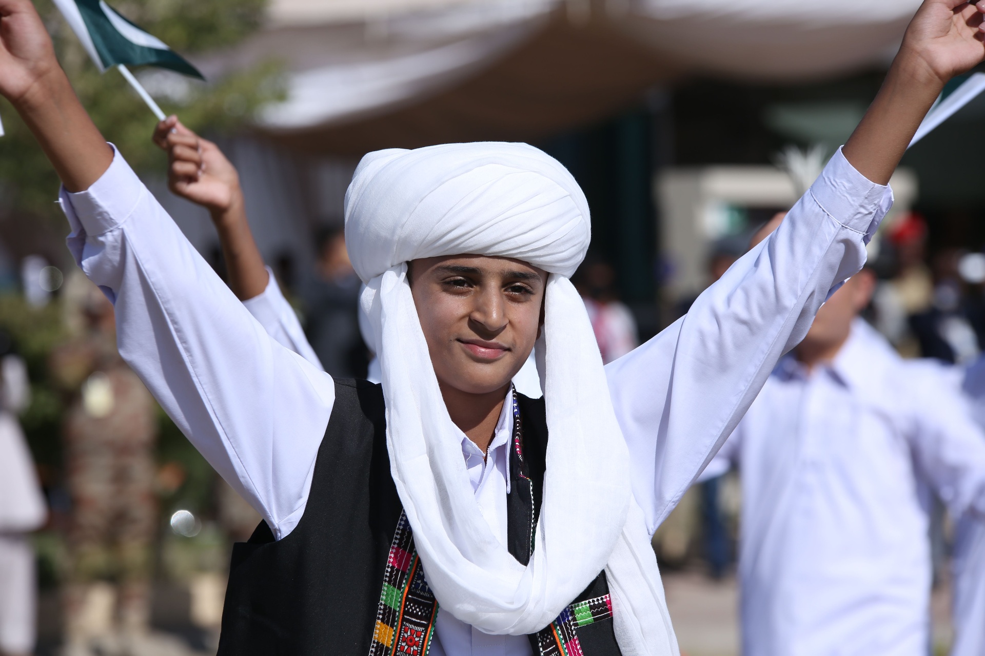 A young Pakistani community member in traditional dress raising the Pakistani flag during a cultural celebration